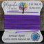 Spool of purple thread on a card with 'Magnolia Bead Company' branding, on a wooden surface.