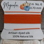 Orange silk thread on a Magnolia label with wooden background