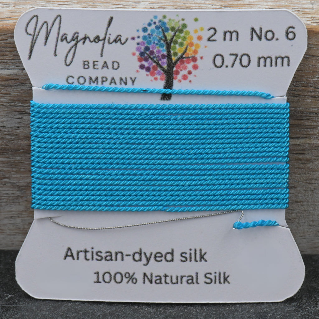 Blue silk thread on a Magnolia Bead Company label against a wooden background