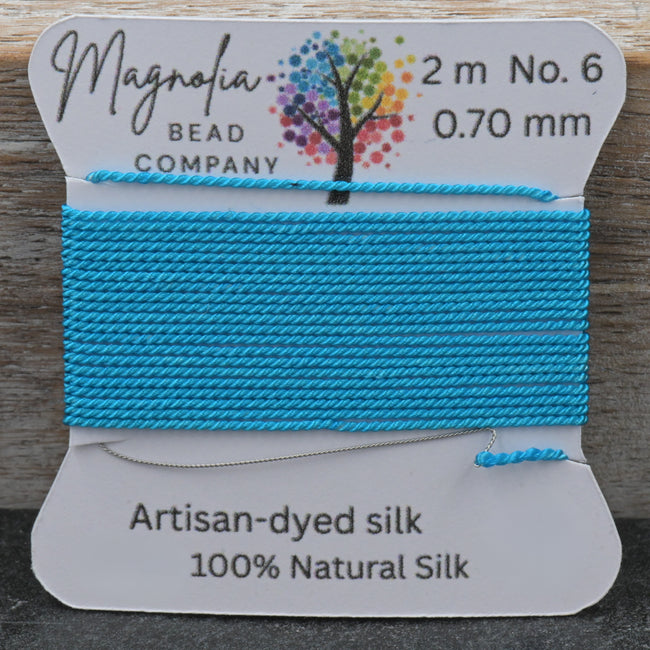 Blue silk thread on a Magnolia Bead Company label against a wooden background Hover Image