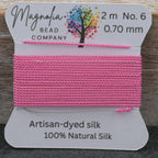 Pink thread on a card with Magnolia Bead Company branding against a wooden background