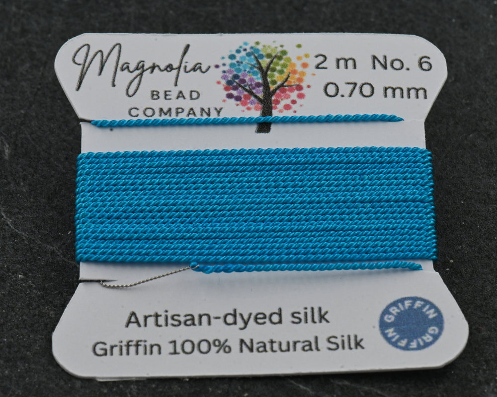 Blue thread spool with Magnolia Bead Company label on a dark background