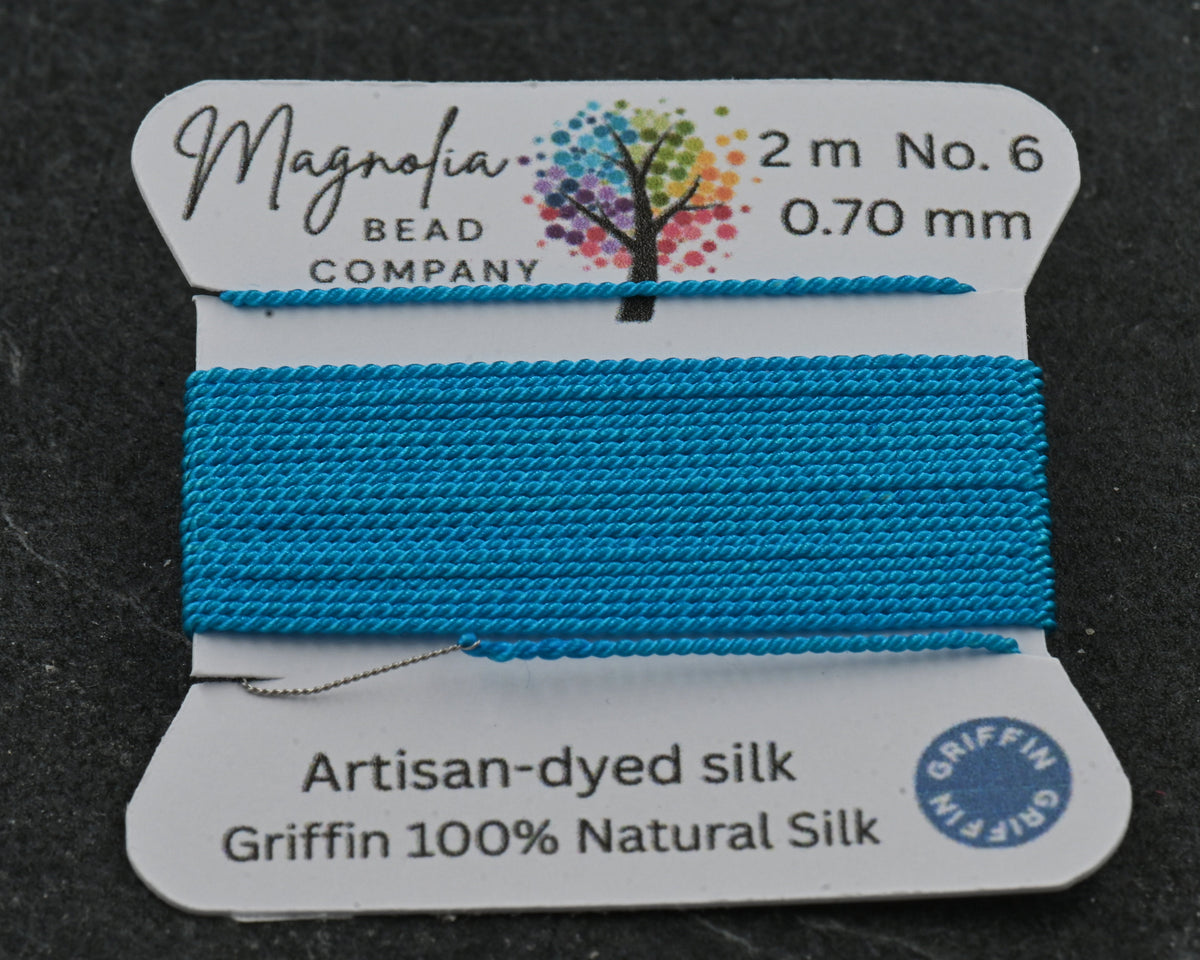Blue thread spool with Magnolia Bead Company label on a dark background