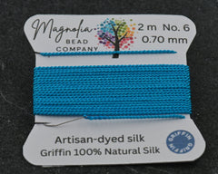 Blue thread spool with Magnolia Bead Company label on a dark background