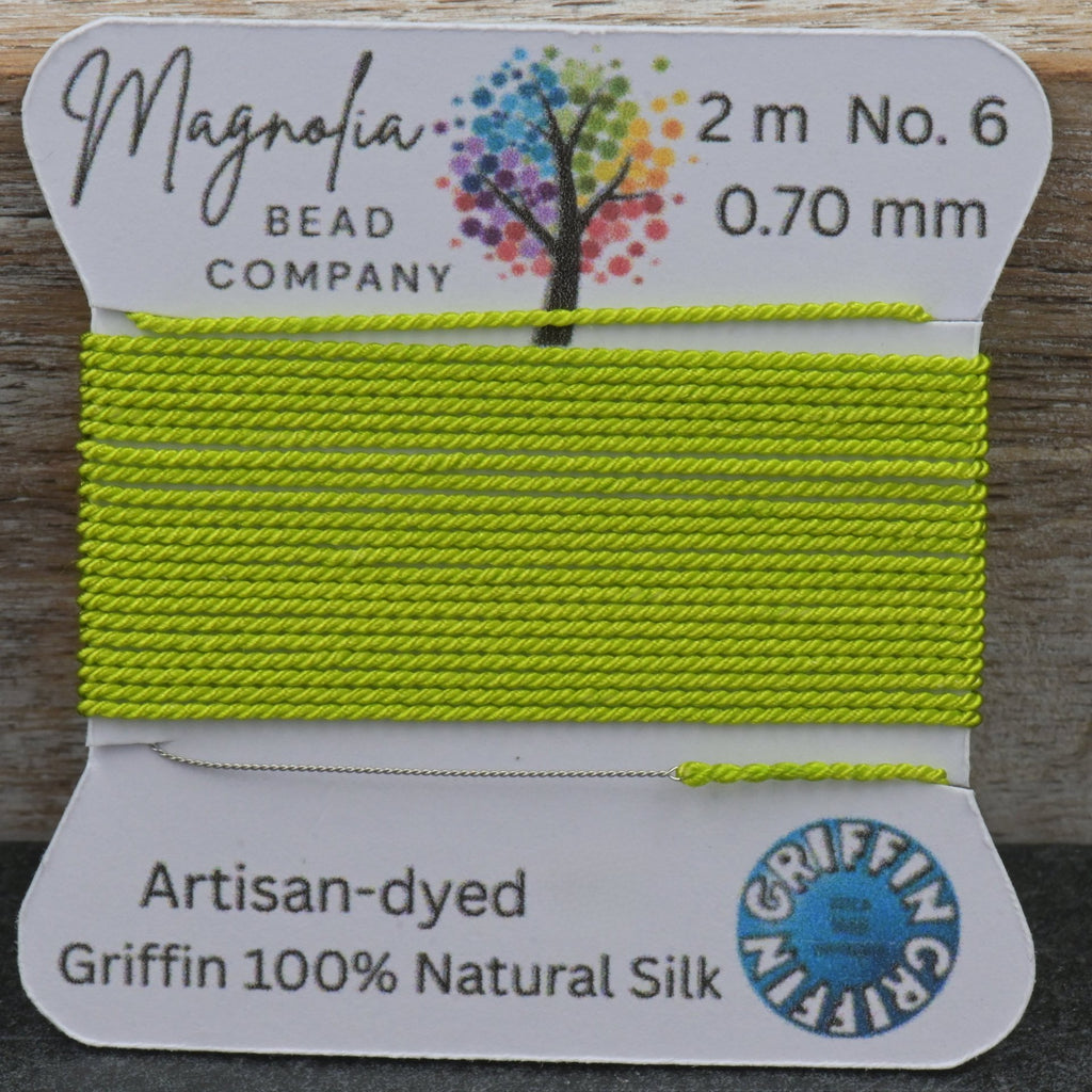Lime green thread on a card with 'Magnolia Bead Company' branding against a wooden background