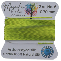 Lime green thread on a card with 'Magnolia Bead Company' branding against a wooden background