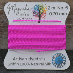 Pink thread on a spool with 'Magnolia Bead Company' label on a wooden background