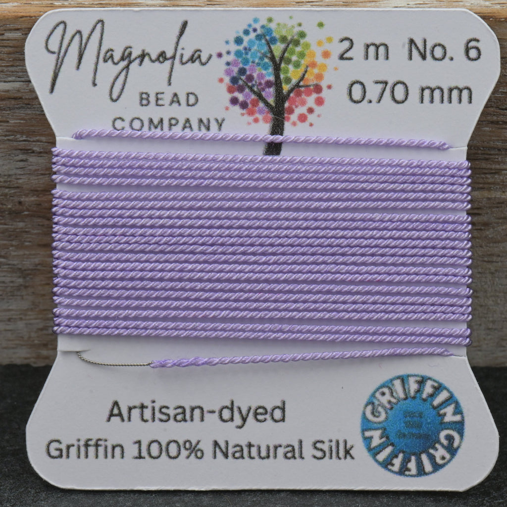 Spool of lavender thread with a label from Magnolia Bead Company on a wooden surface.