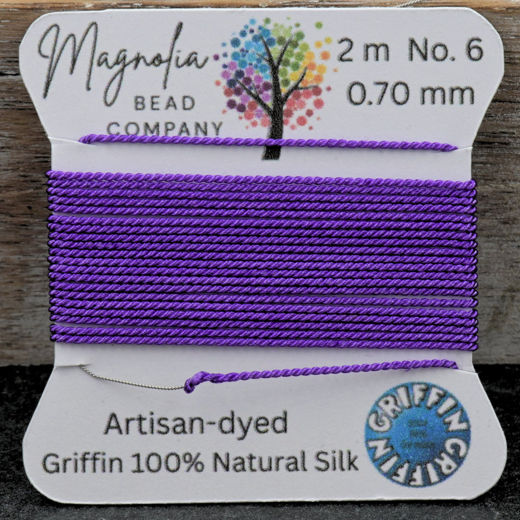 Spool of purple thread on a card with 'Magnolia Bead Company' branding, on a wooden surface.