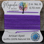 Spool of purple thread on a card with 'Magnolia Bead Company' branding, on a wooden surface.