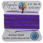 Spool of purple thread on a card with 'Magnolia Bead Company' branding, on a wooden surface.