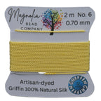 Yellow thread on a card with 'Magnolia Bead Company' branding against a wooden background
