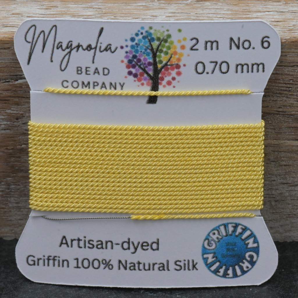 Yellow thread on a card with 'Magnolia Bead Company' branding against a wooden background