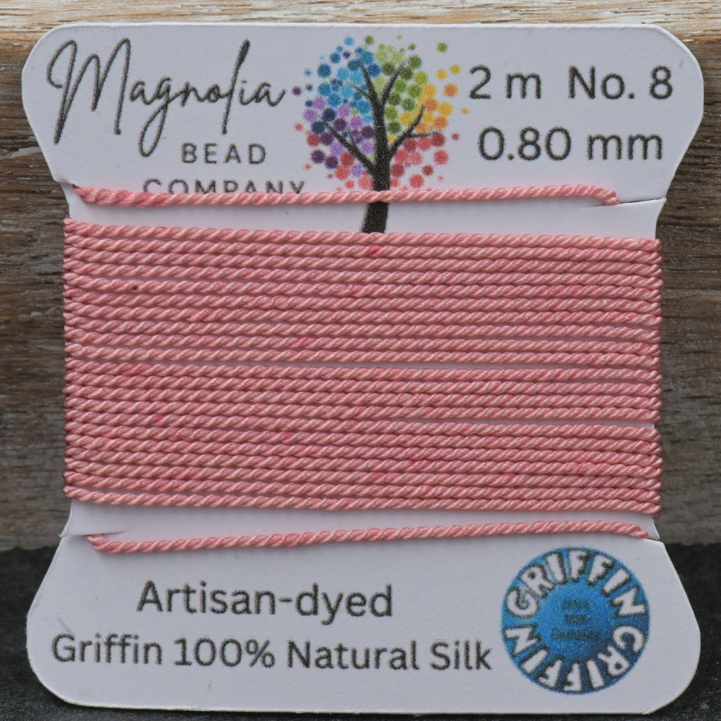 Pink thread on a spool with Magnolia Bead Company label on a wooden surface