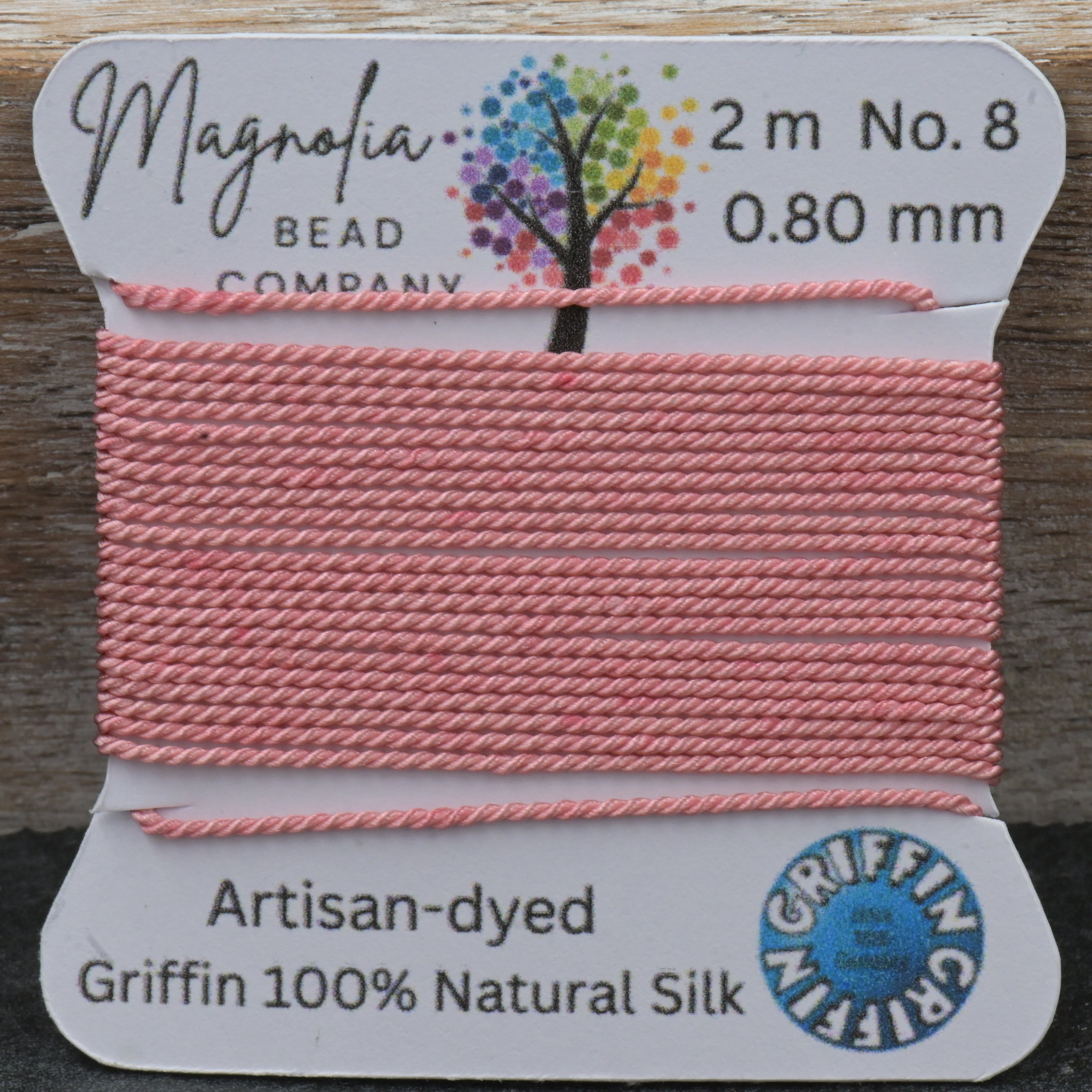 Pink thread on a spool with Magnolia Bead Company label on a wooden surface