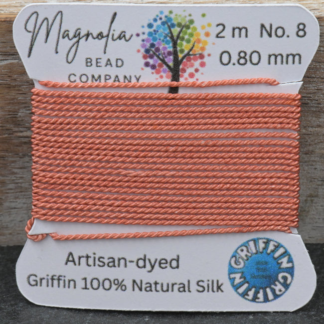 Spool of orange thread with a label from Magnolia Bead Company on a wooden surface. Hover Image