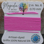 Pink thread on a card with 'Magnolia Bead Company' branding, displayed against a wooden background.