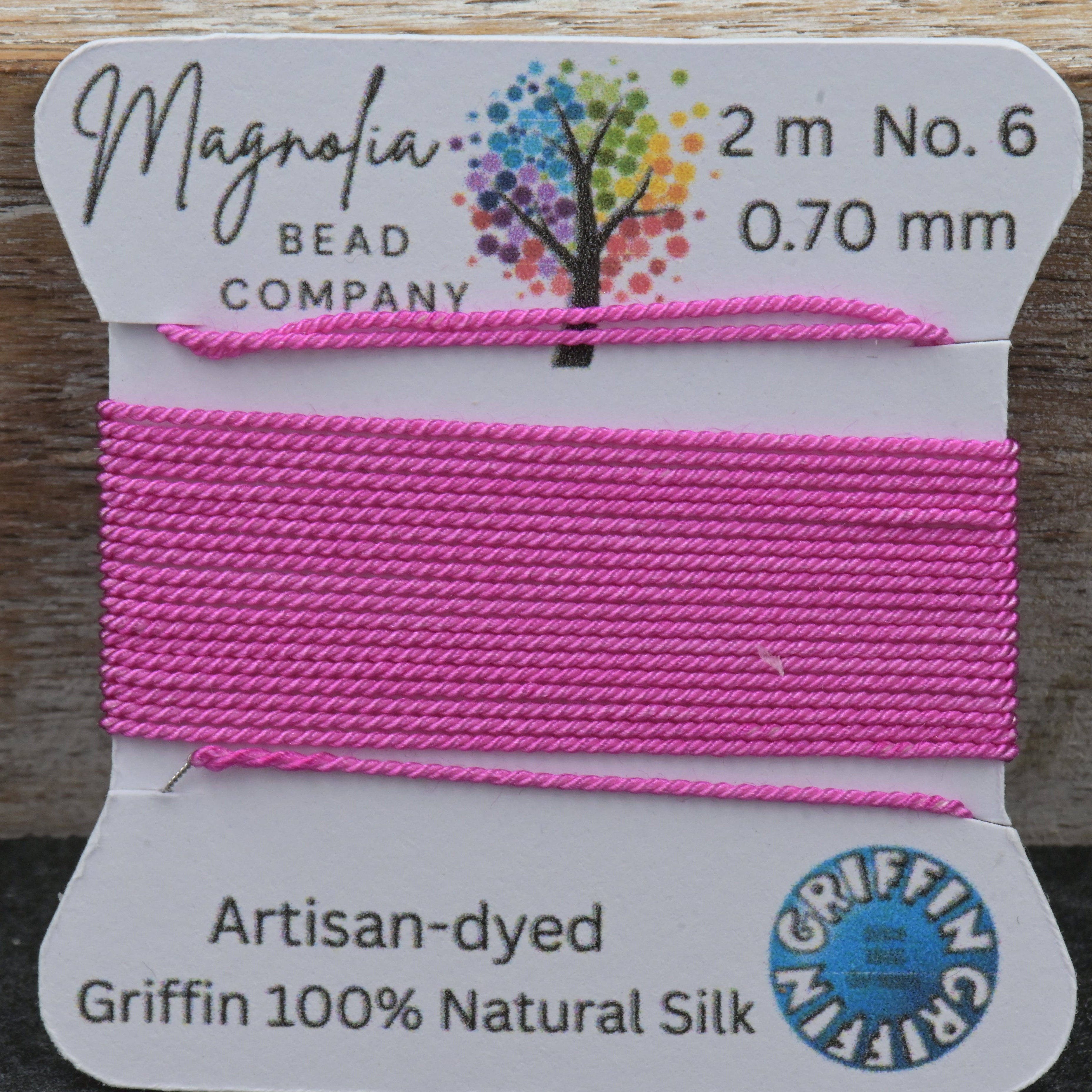 Pink thread on a card with 'Magnolia Bead Company' branding, displayed against a wooden background.