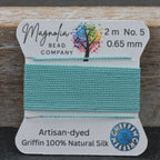 Spool of teal thread with Magnolia Bead Company label on a wooden surface