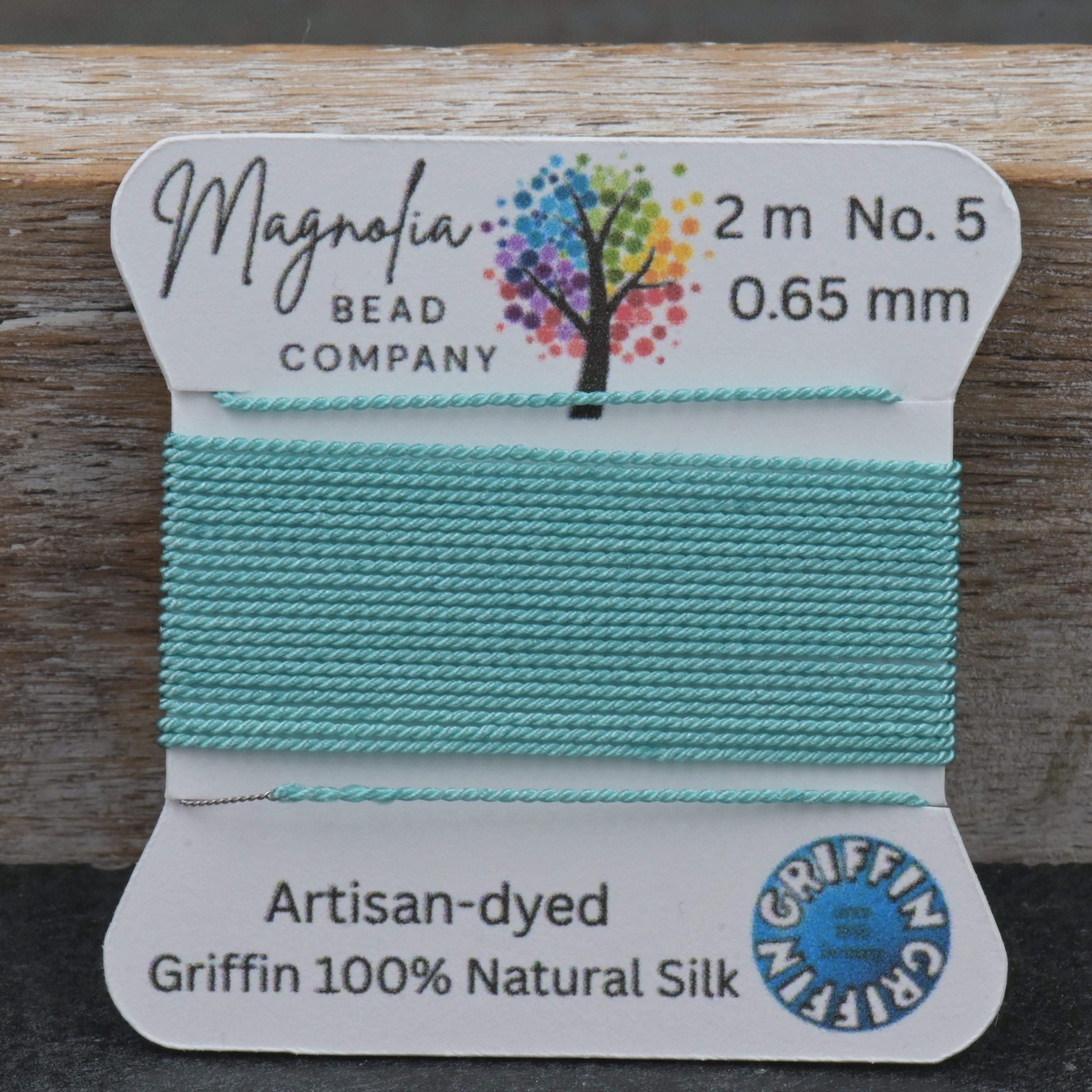 Spool of teal thread with Magnolia Bead Company label on a wooden surface