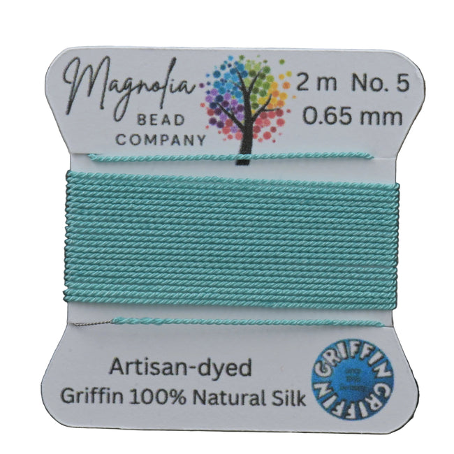 Spool of turquoise thread with Magnolia Bead Company label on a wooden surface Hover Image