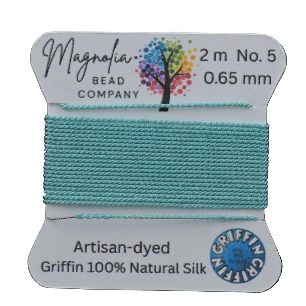Spool of turquoise thread with Magnolia Bead Company label on a wooden surface