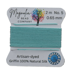 Spool of turquoise thread with Magnolia Bead Company label on a wooden surface