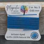 Blue thread on a label with Magnolia Bead Company branding against a wooden background