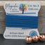 Blue thread on a card with 'Magnolia Bead Company' branding, next to three copper beads on a wooden surface.