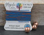 Bead thread with a label from Magnolia Bead Company on a wooden surface