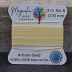 Yellow thread spool with Magnolia Bead Company packaging on a wooden surface