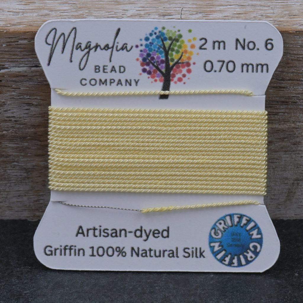 Yellow thread spool with Magnolia Bead Company packaging on a wooden surface