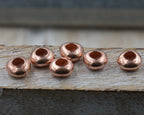 Set of six copper beads on a wooden surface with a blurred background