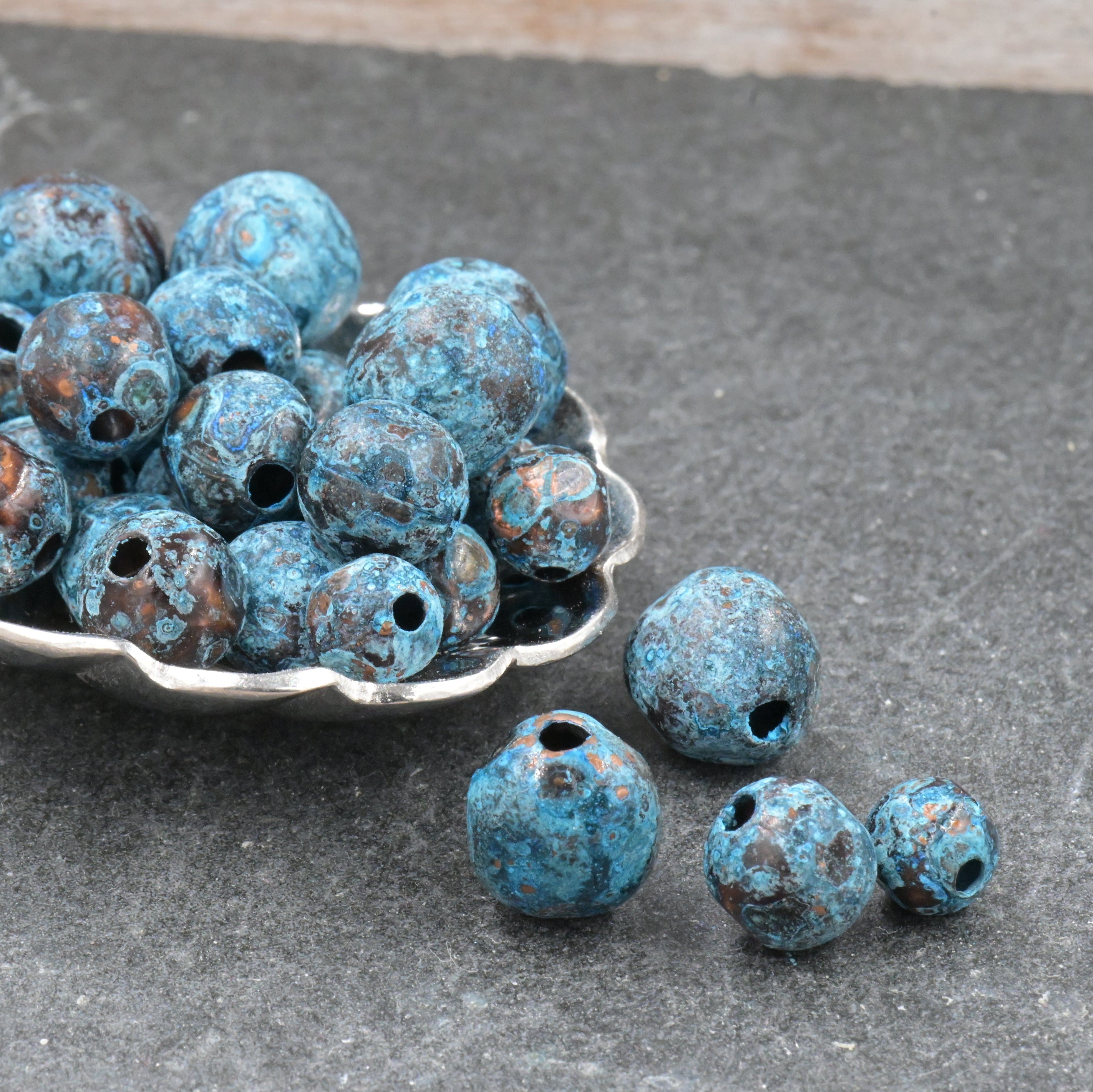 Blue beads in a silver spoon on a gray surface