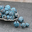 Blue beads in a silver spoon on a gray surface