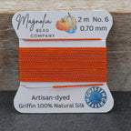 A spool of bright orange beading thread from the Magnolia Bead Company, Griffing Atlantis edition, displayed on a rustic wooden background.