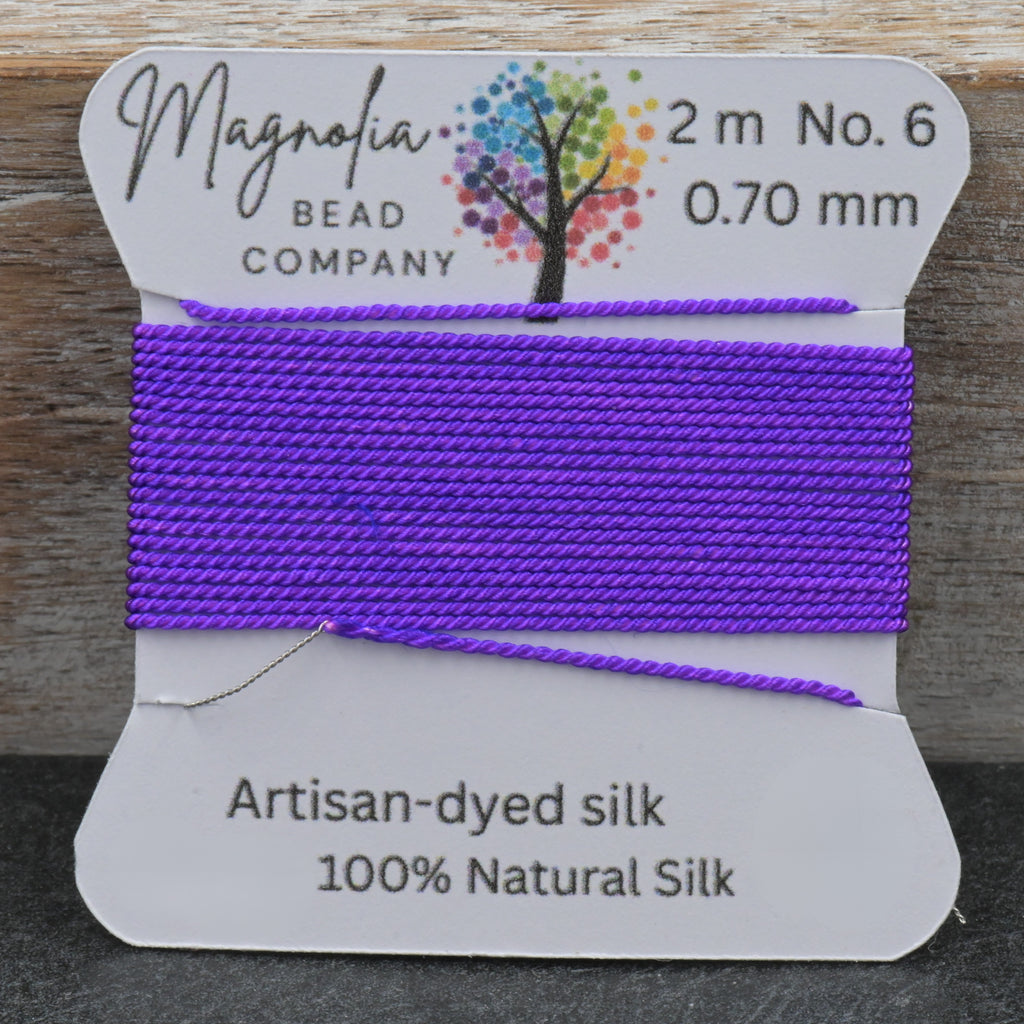 Purple thread on a Magnolia Bead Company label against a wooden background