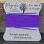 Purple thread on a Magnolia Bead Company label against a wooden background
